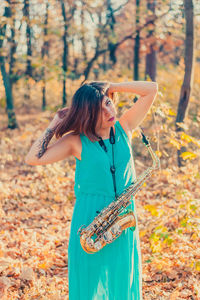 Woman with saxophone standing in forest during autumn