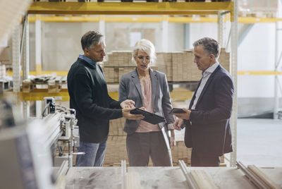 Business people discussing over digital tablet while standing at lumber industry