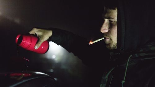 Close-up of man pouring drink in container while smoking at night outdoors