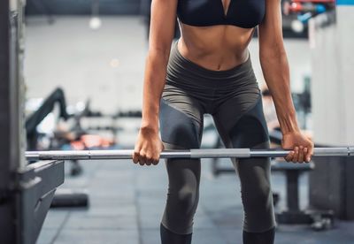 Midsection of young woman lifting dumbbell in gym
