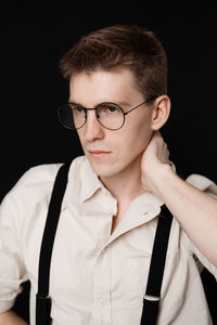 Close-up of young man wearing eyeglasses looking away against black background