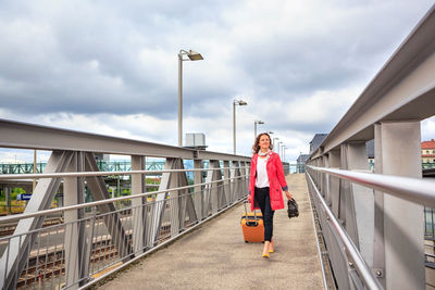 Smiling mid adult woman walking with suitcase on footbridge