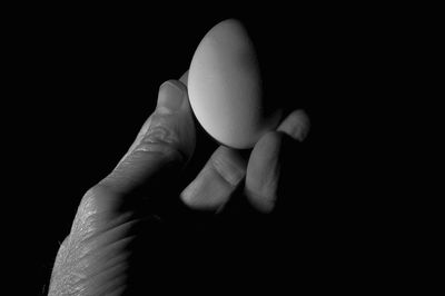 Cropped hand holding egg against black background