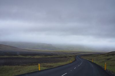 Empty road amidst landscape against cloudy sky