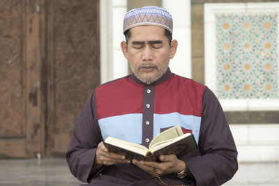 Mature man reading koran while sitting at mosque