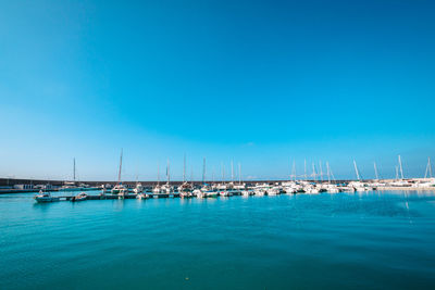 Sailboats moored in sea against blue sky