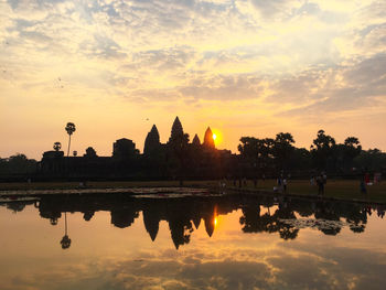 Scenic view of lake by buildings against sky during sunset