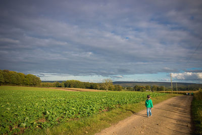 Rear view of boy walking on field against sky