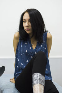 Woman looking away while sitting against wall