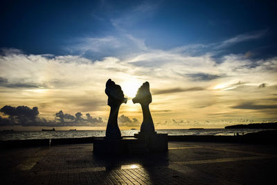 Silhouette statue by sea against sky during sunset