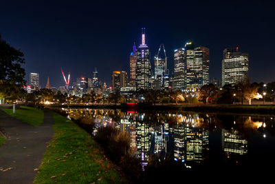 Illuminated buildings by river against sky at night