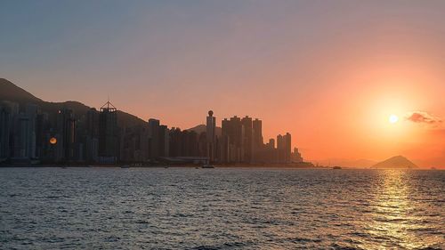 Sea by buildings against sky during sunset