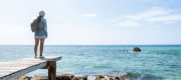 Rear view of woman standing on rock by sea against sky