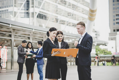 Business people discussing over file while standing outdoors