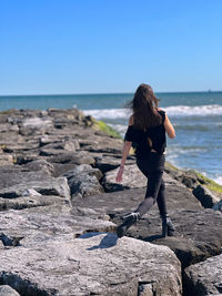 Rear view of woman standing at beach against clear sky