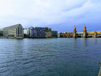 View of buildings by river against cloudy sky