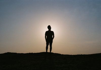 Silhouette man standing on land against sky during sunset