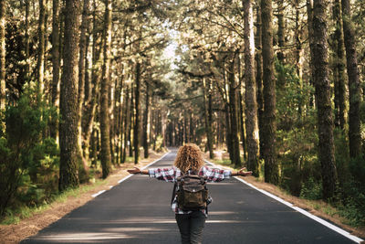 Rear view of woman walking on road amidst trees