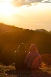 Rear view of couple sitting on land against sky during sunset