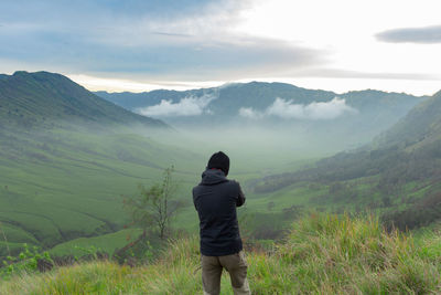 Rear view of man standing on mountain against sky