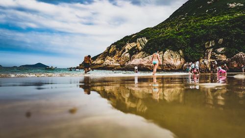 People enjoying on beach by rock formation against sky