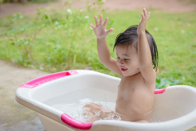 Cute baby girl looking away while sitting in bathtub at yard