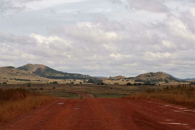 Country road along landscape and mountains against cloudy sky