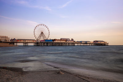 Ferris wheel on beach against sky during sunset