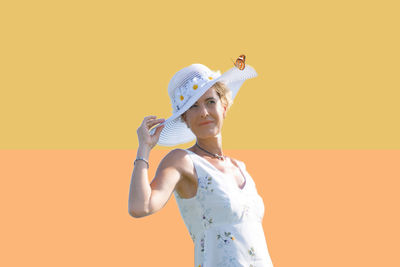 Mature woman wearing sun hat standing against wall