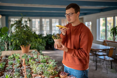 Man taking picture photo of potted plants in floral shop market on smartphone.