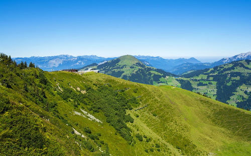 Scenic view of green landscape and mountains against clear blue sky