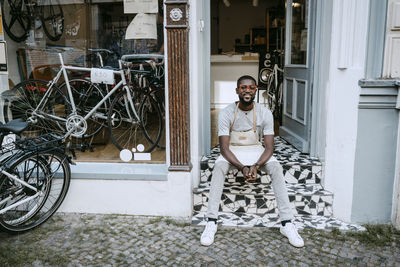 Portrait of male owner sitting on steps of bicycle shop