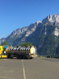 Vehicles on road against mountain range against clear blue sky