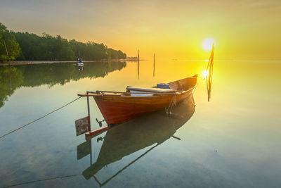 Boat moored in lake against sky during sunset