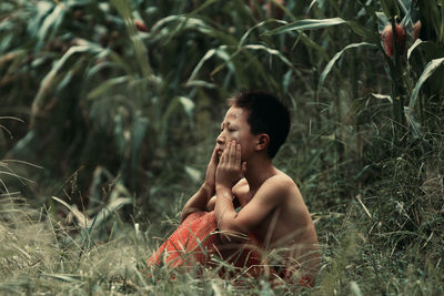 Boy looking away while sitting on land