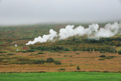 Smoke emitting from chimney on field against sky