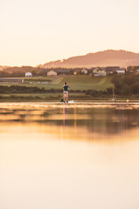 Man on lake against clear sky during sunset