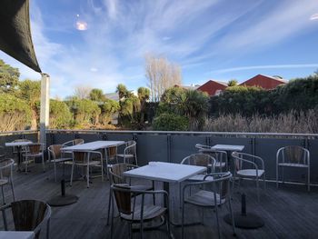 Empty chairs and tables in cafe against sky