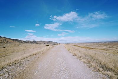 Road amidst field against blue sky