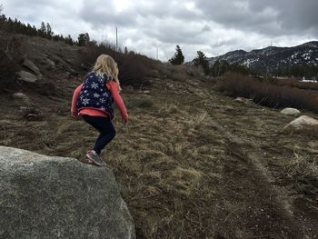 Rear view of girl on rock at field against cloudy sky during winter