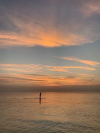 Silhouette person in sea against sky during sunset