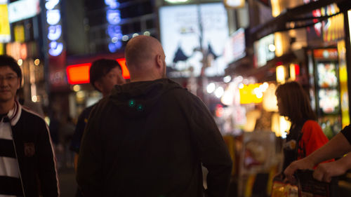 Rear view of people standing on illuminated street at night