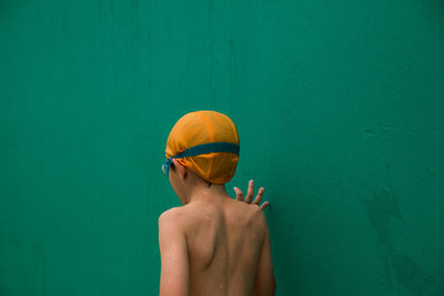 Rear view of wet shirtless boy standing against green wall