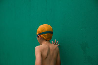 Rear view of shirtless boy standing against wall