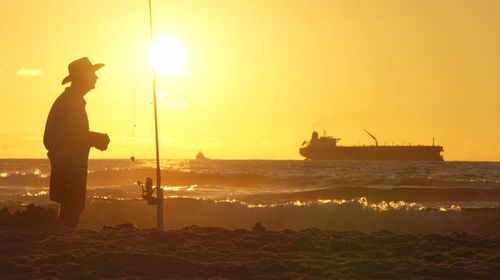 Silhouette man standing with fishing rod on beach against clear sky during sunset