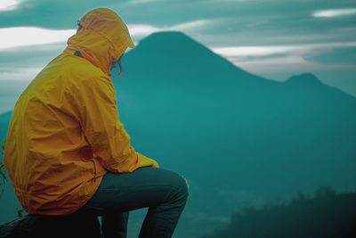 Side view of man sitting on mountain by lake