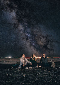 Friends sitting on field against star field at night