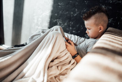 Side view of boy relaxing on bed at home
