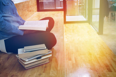 Midsection of woman with books sitting on wooden floor