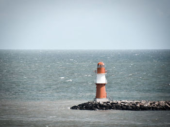 Lighthouse by sea against clear sky